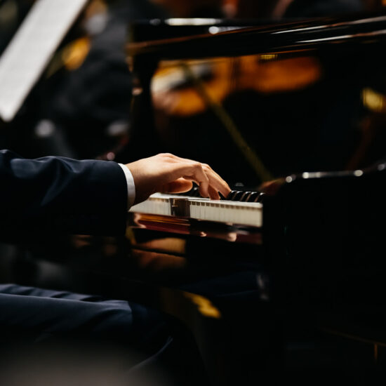 Pianist playing a piece on a grand piano at a concert, seen from the side.