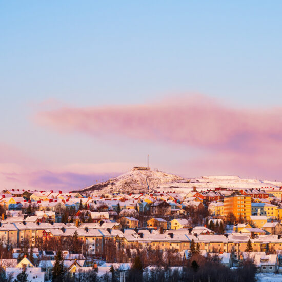 Kiruna skyline, Sweden, in winter with orange and red hues from the low sun. Snow. Colorful houses. Ski slopes.