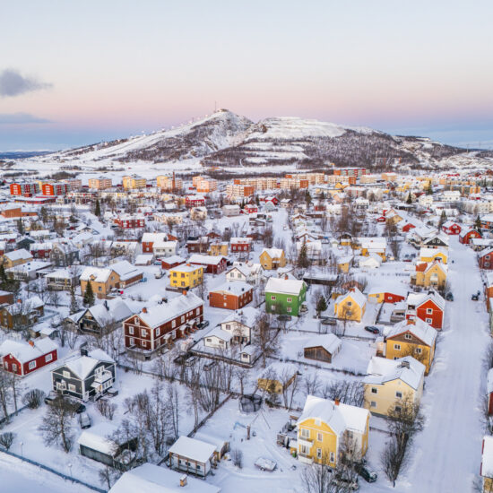 Kiruna, Sweden, colorful houses in a wintry landscape in the high arctic during the polar night, mountains and ski slopes in the distance