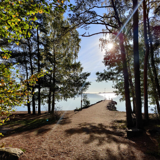 Scenic waterfront path in Espoo, Finland, with a gravel trail leading to a pier on the northern shore of the Gulf of Finland. Calm coastal landscape blending nature and urban life