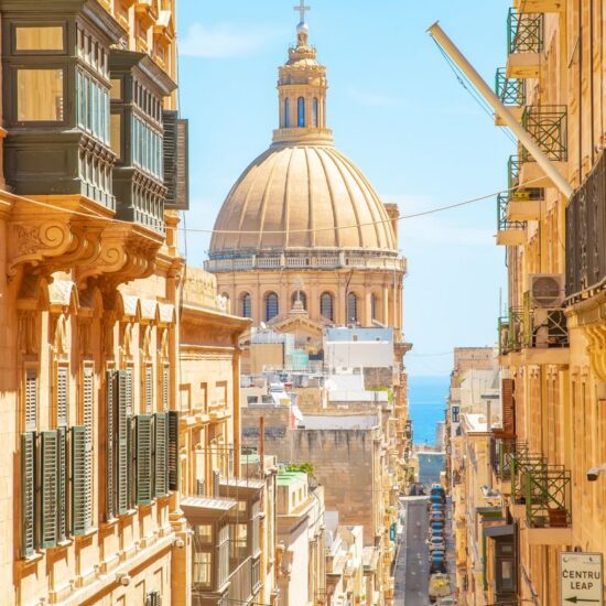 Sunny street in Valletta old town, Basilica of Our Lady of Mount Carmel on a background, Malta