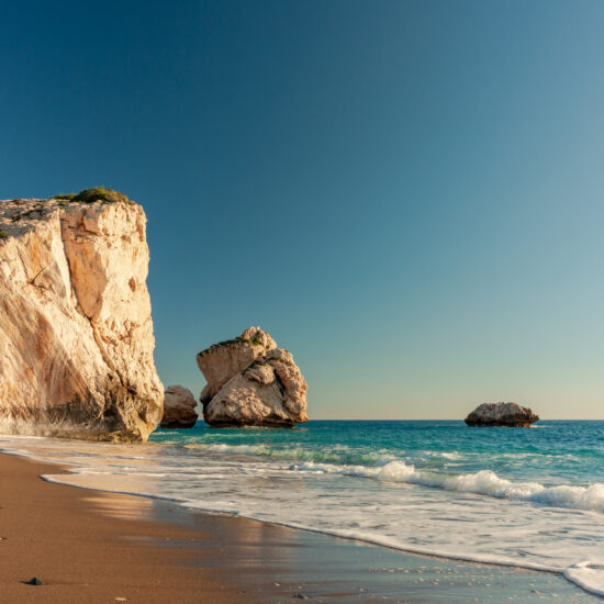Golden Petra tou Romiou cliffside Aphrodite's beach with Aphrodite's rock formations and calm turquoise sea under clear sky