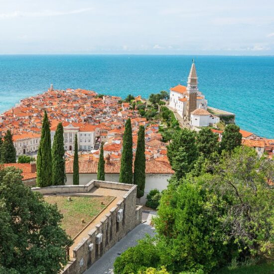 The coastal town of Piran in Slovenia, a picturesque seaside landscape, seen from the Walls of Piran tourist attraction. Colorful buildings surrounded by blue water.